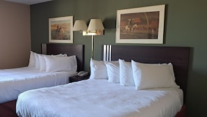 Een hotelkamer met twee bedden, een nachtkastje, een lamp en twee ingelijste foto’s aan de muur.