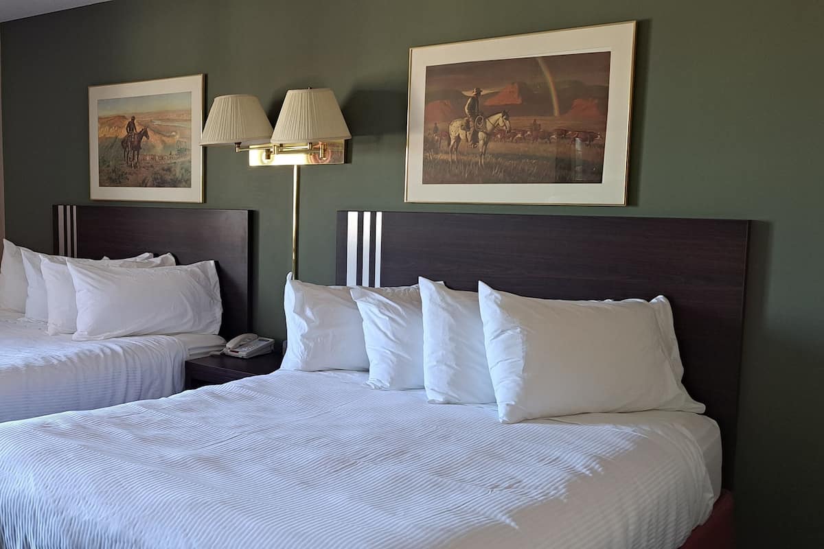 Une chambre d’hôtel avec deux lits, une table de chevet, une lampe et deux tableaux encadrés au mur.