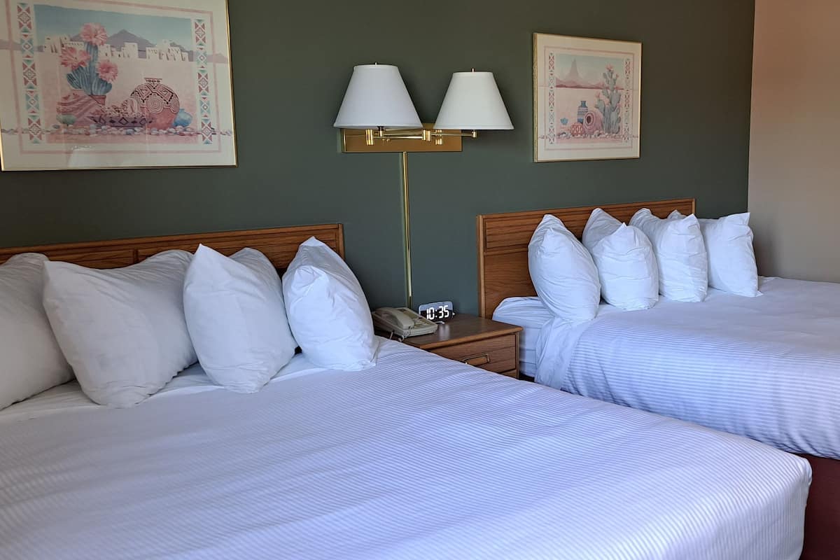 Une chambre d’hôtel avec deux lits, une table de chevet avec une lampe et deux tableaux encadrés au mur.