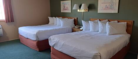 A hotel room with two beds, a nightstand, a lamp, and artwork on the walls.