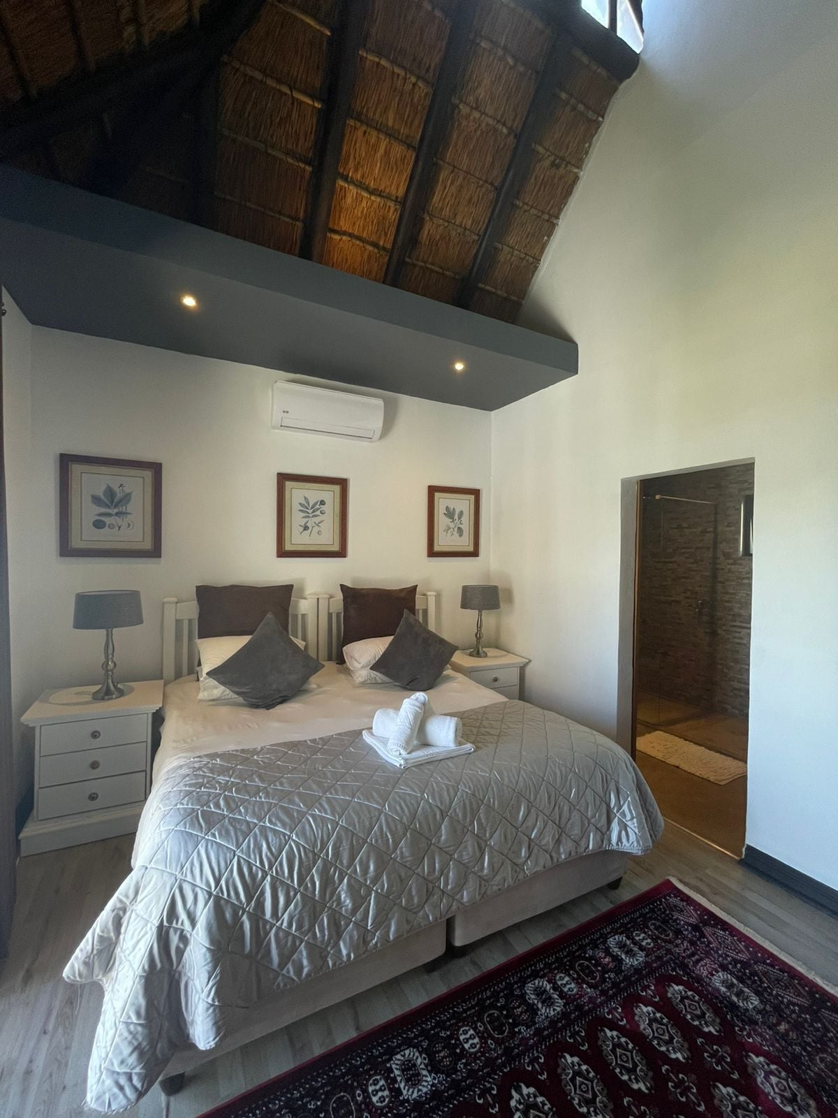 Een slaapkamer met een groot bed, twee nachtkastjes, een wandairconditioner en een deur naar een badkamer.