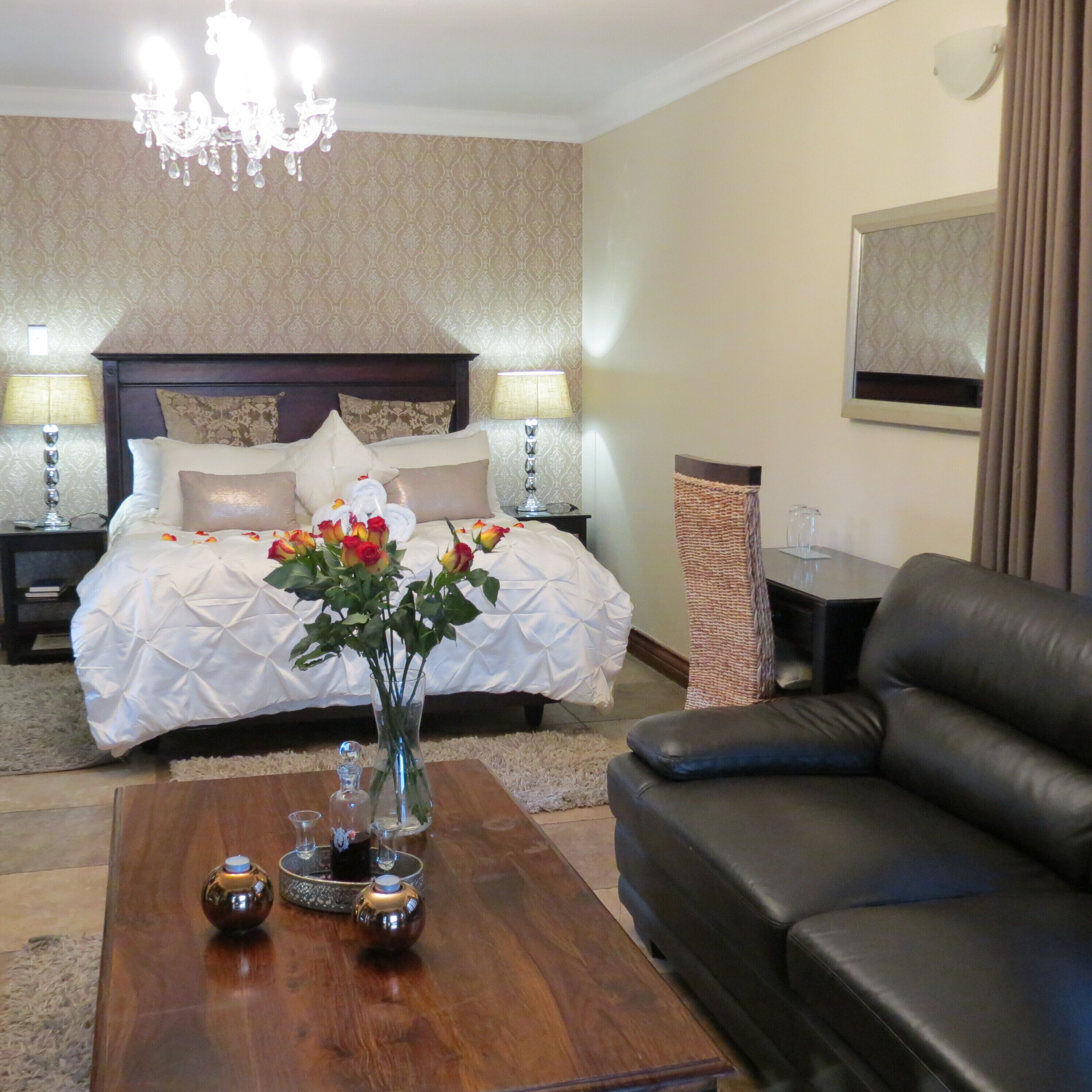 Habitaci ón de hotel con una cama grande, dos lámparas de noche, una araña, un jarrón con flores, un sofá de cuero y una mesita con objetos decorativos.
