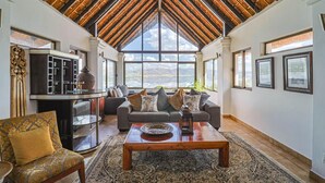A spacious living room with a high ceiling, a large window offering a view of the mountains, a sofa set, and a coffee table. - Galagos Lodge (Hartbeespoort)