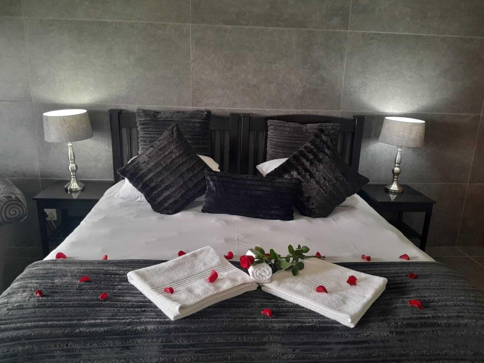 Een keurig opgemaakt bed met kussens, een opgevouwen handdoek en rozenblaadjes.