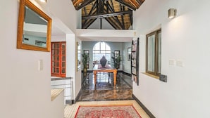 A hallway with a high ceiling, a red-framed mirror, a patterned rug, and a view through a large window. - Galagos Lodge (Hartbeespoort)
