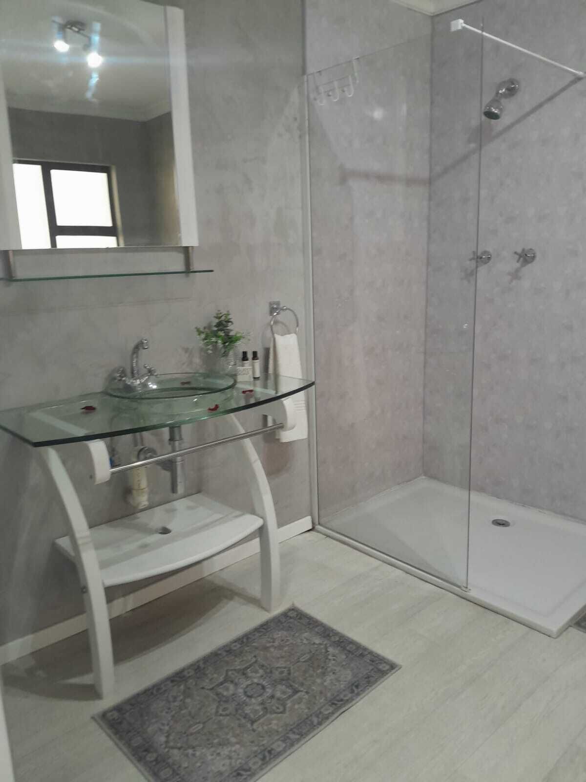 A bathroom with a glass sink, a mirror, a shower, and a rug.