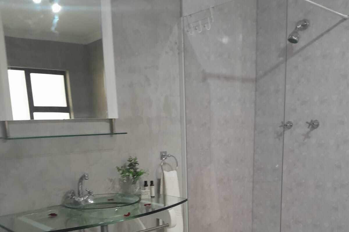 A bathroom with a glass sink, a mirror, a shower, and a rug.