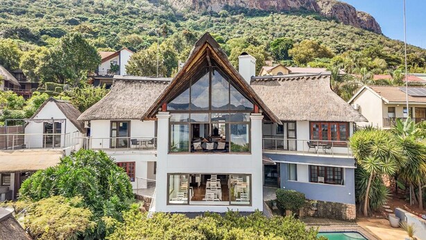 A two-story house with a large balcony, surrounded by lush greenery and mountains in the background. - Galagos Lodge (Hartbeespoort)