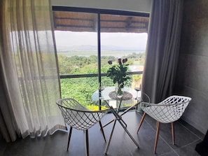 A balcony with two white wire chairs, a small table, and a vase with flowers.