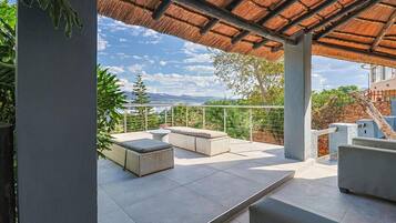 Um alpendre coberto com vista para montanhas, um sofá branco e uma mesa de jantar.