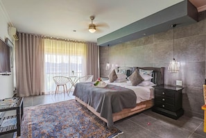 A bedroom with a bed, bedside tables, a desk, a chair, a rug, and a window with curtains. - Galagos Lodge (Hartbeespoort)