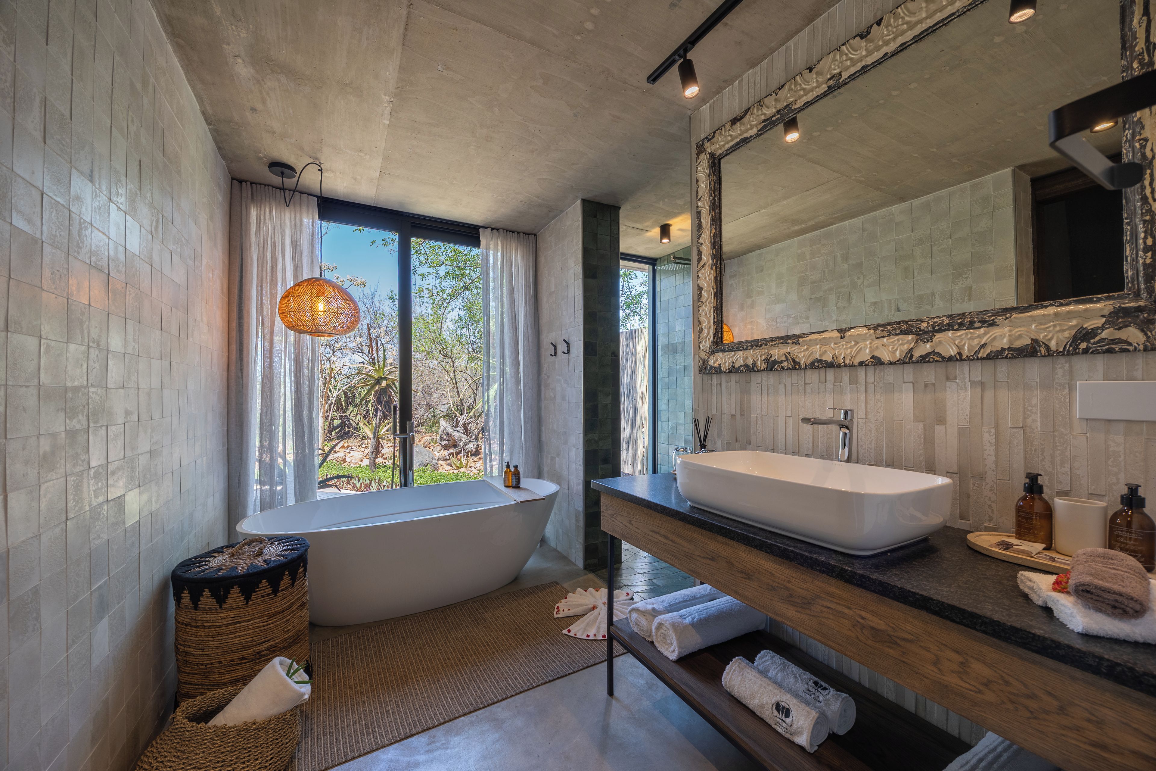 A modern bathroom with a freestanding bathtub, a vanity with a large mirror, and a view of greenery outside.
