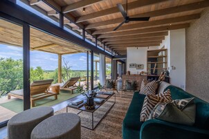 Uma sala de estar ampla com uma grande janela, um sofá verde e teto de madeira.