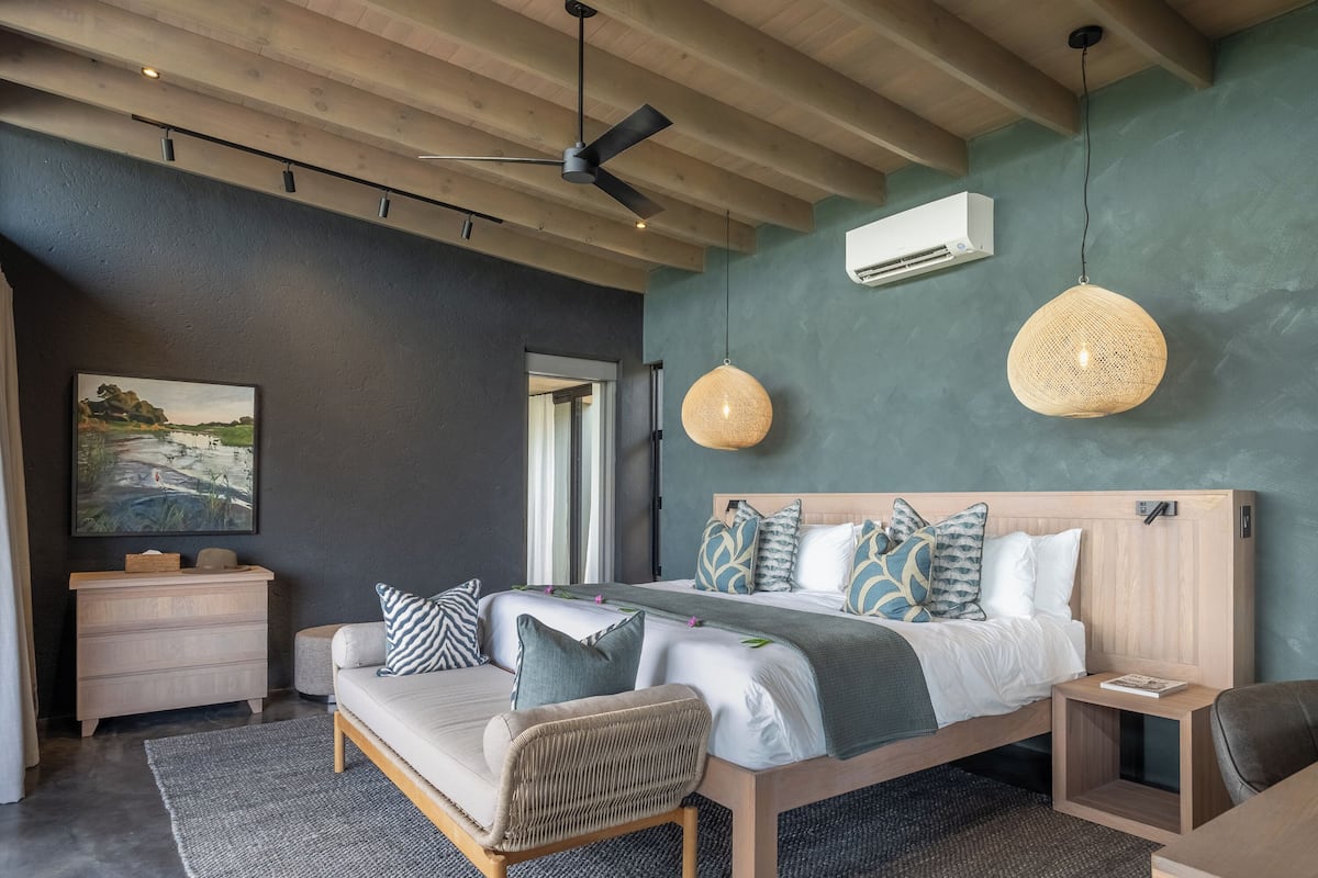A modern bedroom with a wooden bed, a sofa, a small table, and a wall-mounted air conditioner.