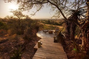 A wooden deck leading to a seating area with chairs and a table, surrounded by natural vegetation and trees. - Klaserie Drift Misava (Bushbuckridge)