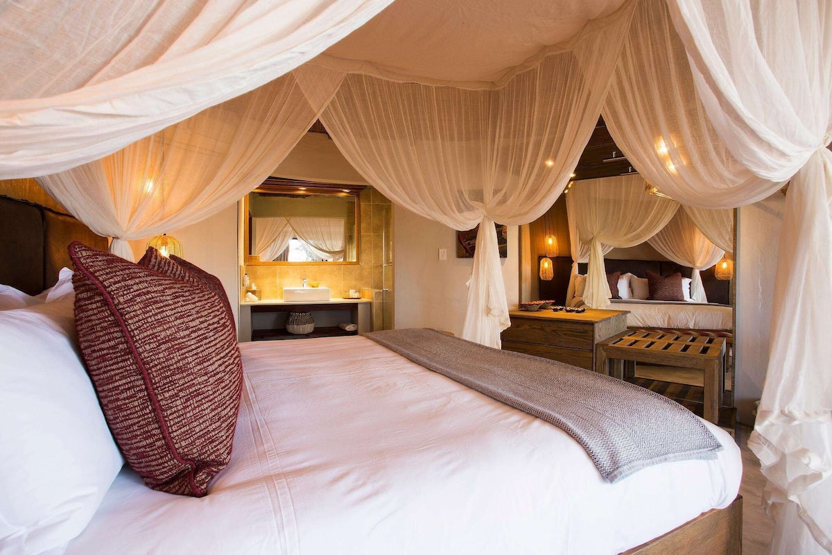 A bedroom with a large bed, a bedside table, a mirror, and a canopy.