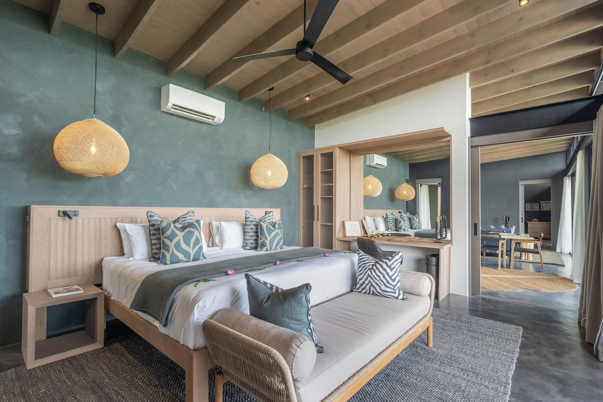 A modern bedroom with a wooden headboard, a large bed with patterned pillows, a bedside table, and a ceiling fan.