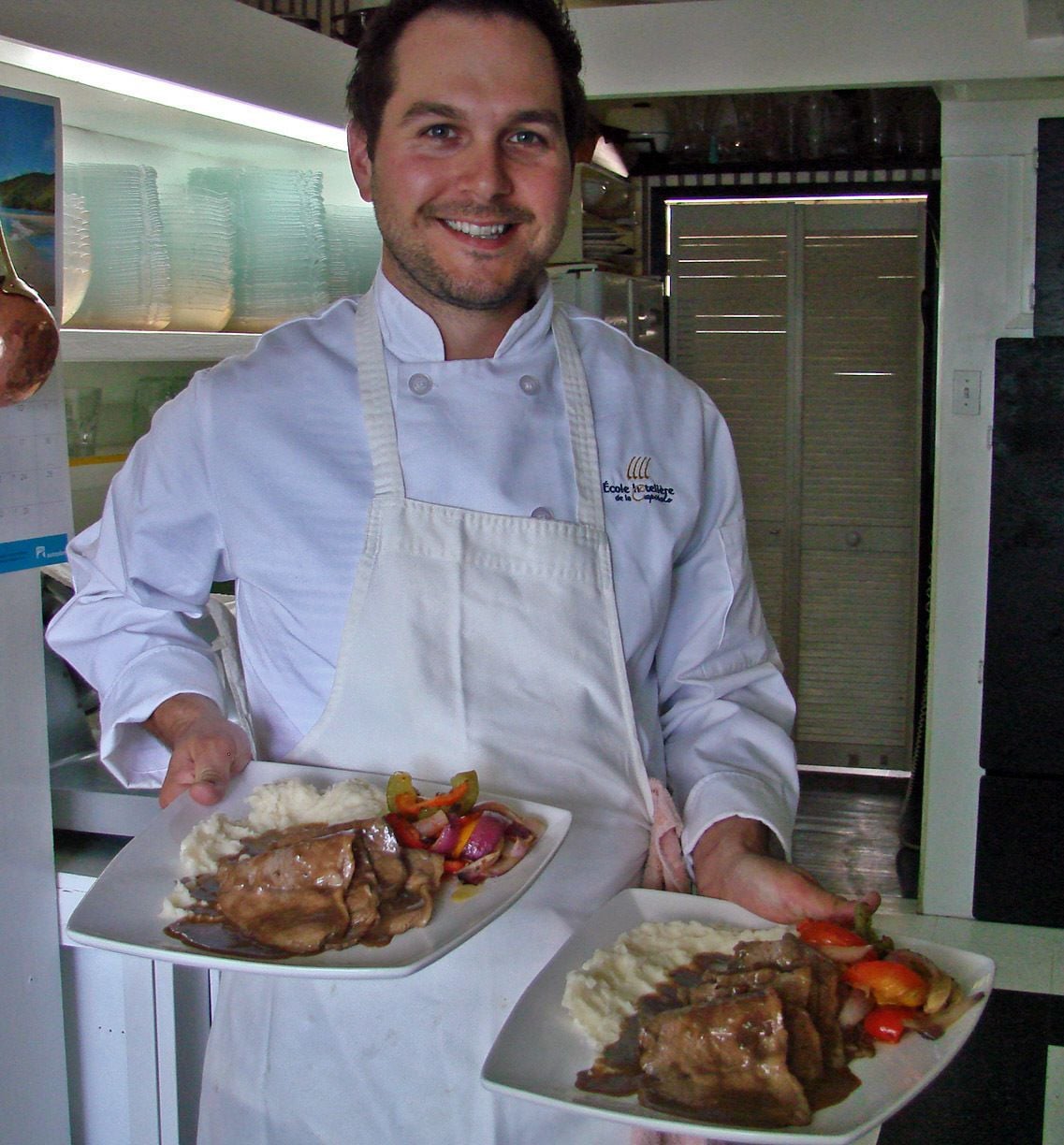 A chef in a white uniform holding two plates of food.