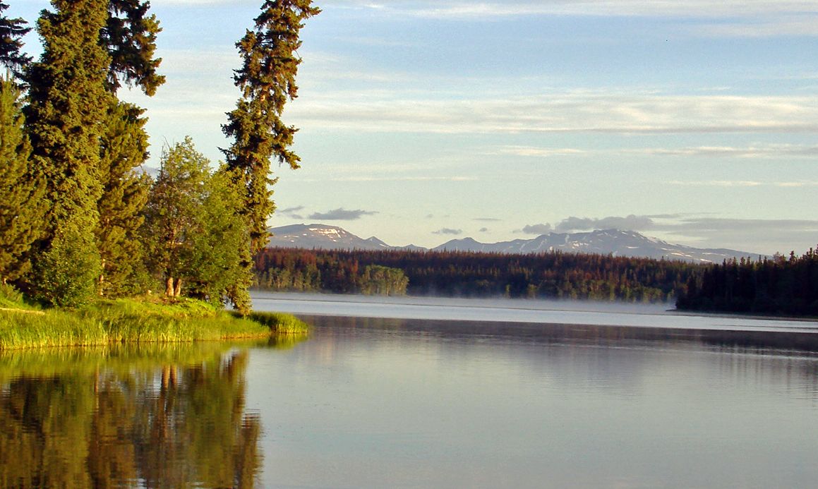 Un lac paisible, entouré d’une forêt dense, avec des montagnes en arrière-plan.