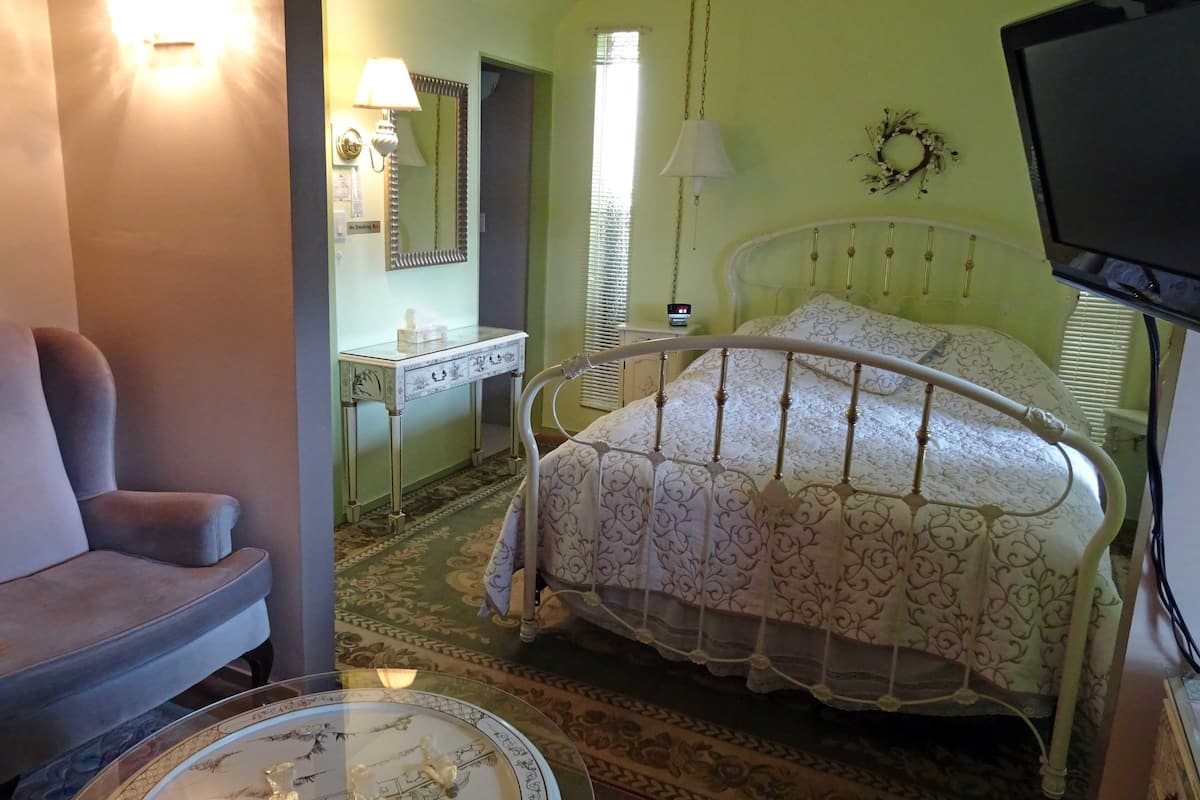 Une chambre à coucher comprenant un lit, une chaise, une table de chevet, une lampe, un miroir et un téléviseur.