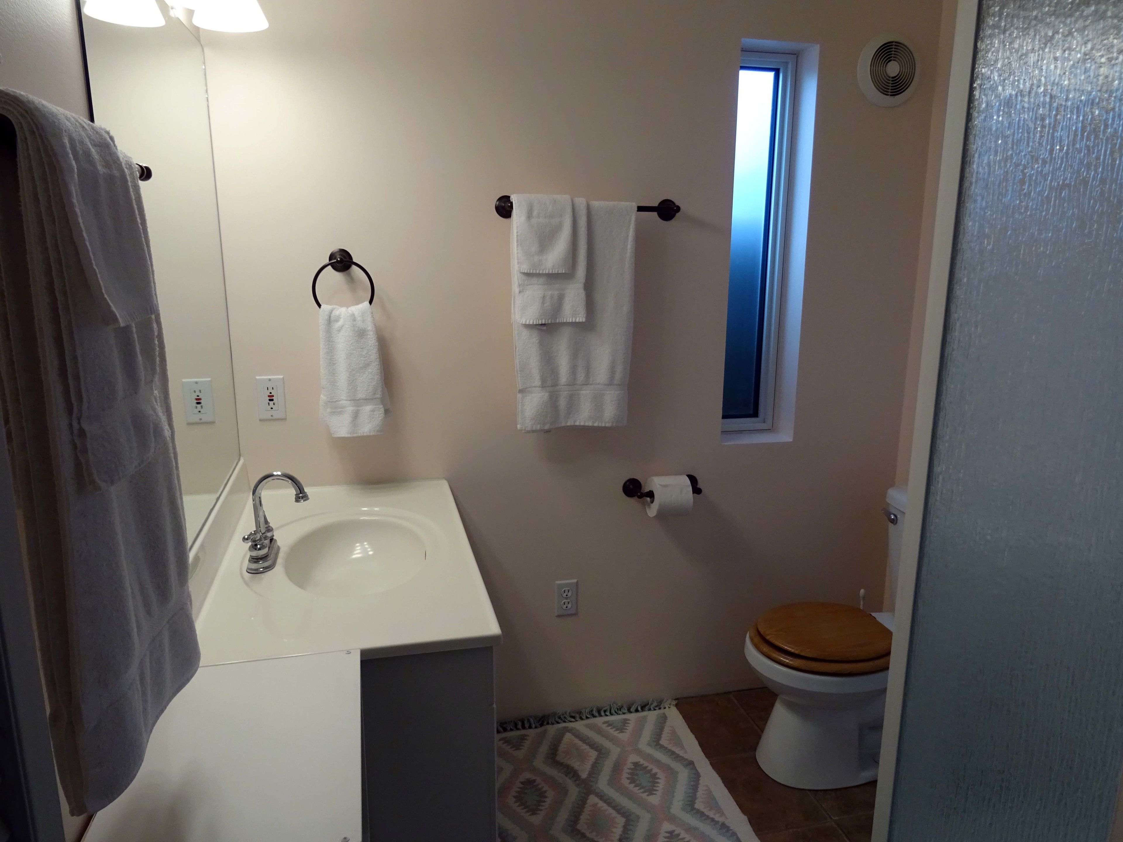 A bathroom with a white sink, a wooden toilet, and two towels hanging on hooks.