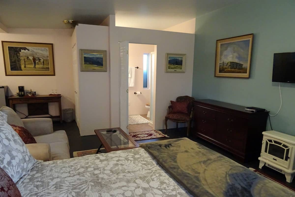 Une chambre d’hôtel équipée d’un lit, d’un bureau, d’une chaise, d’une télévision et décorée avec des œuvres d’art aux murs.
