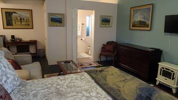 A hotel room with a bed, a desk, a chair, a TV, and artwork on the walls.
