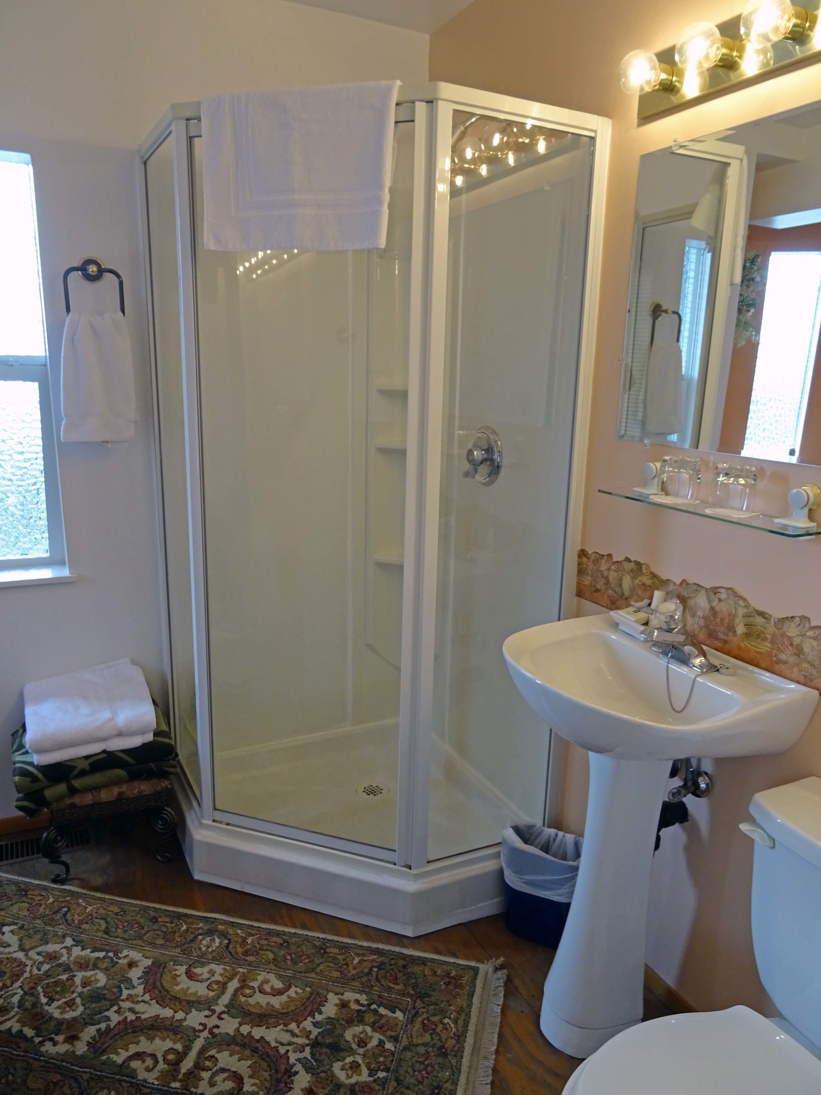 Un baño con ducha envuelta en vidrio, lavabo sobrepedal, inodoro y espejo con iluminación superior.