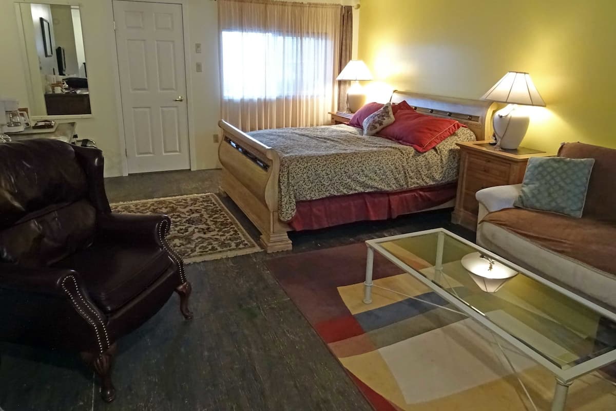 Une chambre d’hôtel comprenant un lit, un fauteuil en cuir, un canapé, une table basse en verre et une table de chevet avec des lampes.