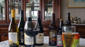 Une table avec différentes bouteilles de vin et de bière, un verre de vin rouge et une canette de bière.