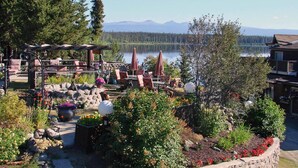 Un espace extérieur aménagé avec des jardinières en pierre, des tables et des chaises, offrant une vue sur un lac et des montagnes en arrière-plan.