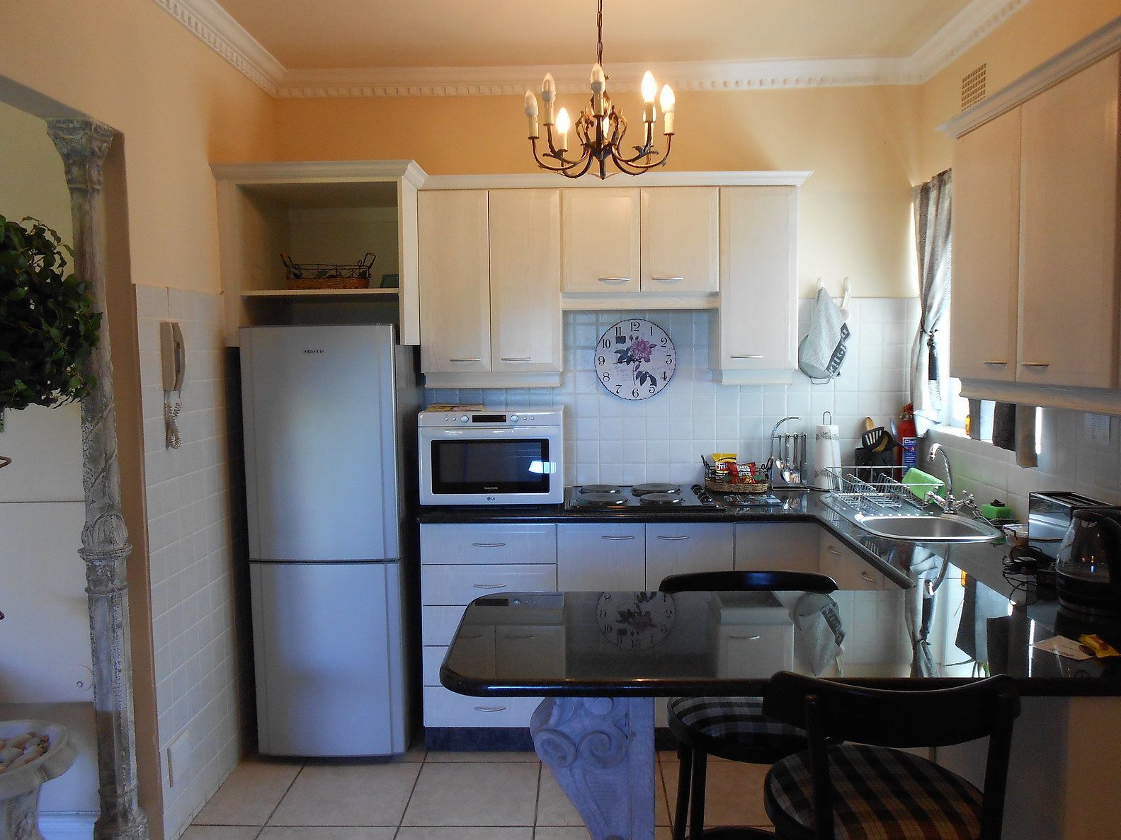 Cocina compacta con armarios blancos, refrigerador, horno, microondas, lavamanos y un comedor con mesa y sillas.