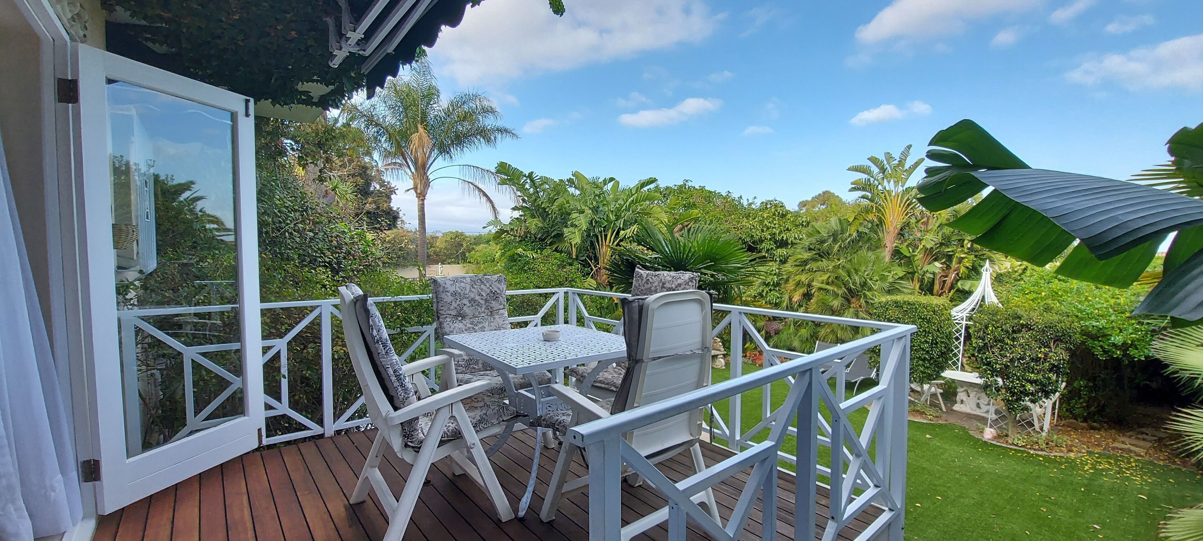 A deck with a table and chairs, surrounded by lush greenery and a clear sky.