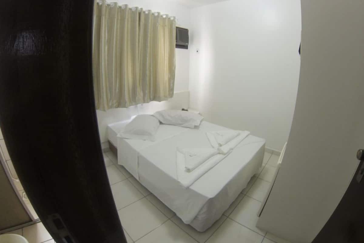Una habitación pequeña y limpia con una cama individual, una ventana con cortinas y una pared blanca.