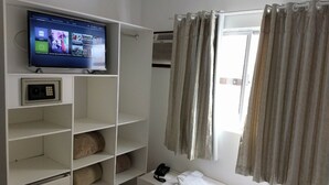 A hotel room with a TV on the wall, a bed, a wardrobe, and a window with curtains. - Master Hotel (Balneário Camboriú)