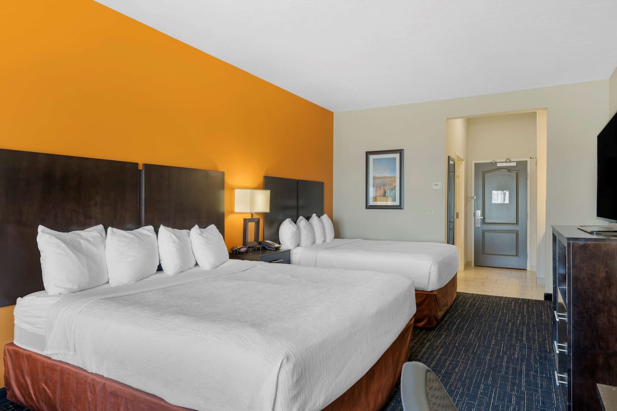 A hotel room with two beds, a desk, a TV, and a door leading to another room.
