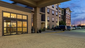 A hotel entrance with a brick facade, large windows, and a parking area with cars. - Best Western Plus North Platte Inn & Suites (North Platte)