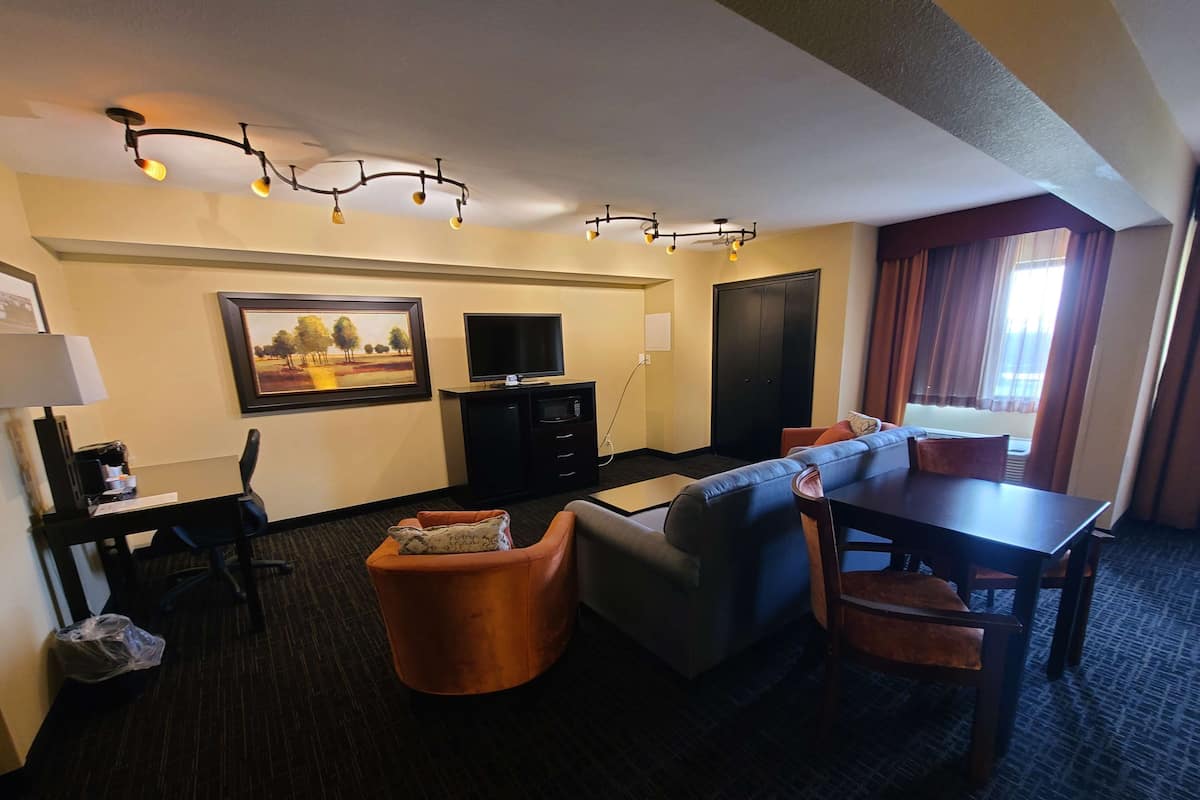 A hotel room with a sofa, armchair, dining table, TV, and artwork on the wall.