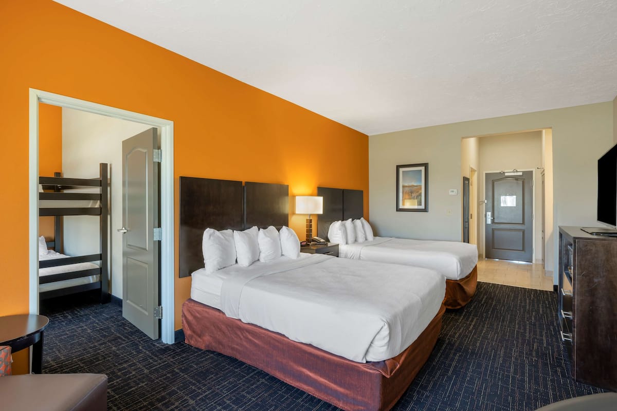 A hotel room with two beds, a desk, a chair, and a TV.