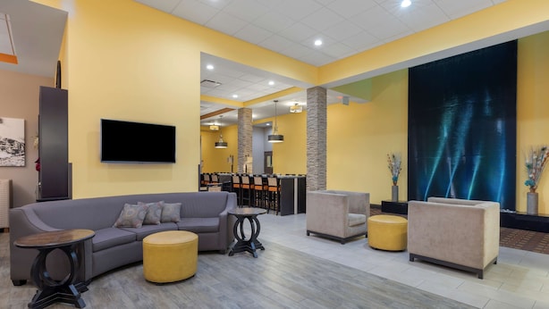 A modern lobby with a sofa, armchairs, and a coffee table. There is a flat-screen TV mounted on the wall and a large digital screen displaying abstract patterns. - Best Western Plus North Platte Inn & Suites (North Platte)