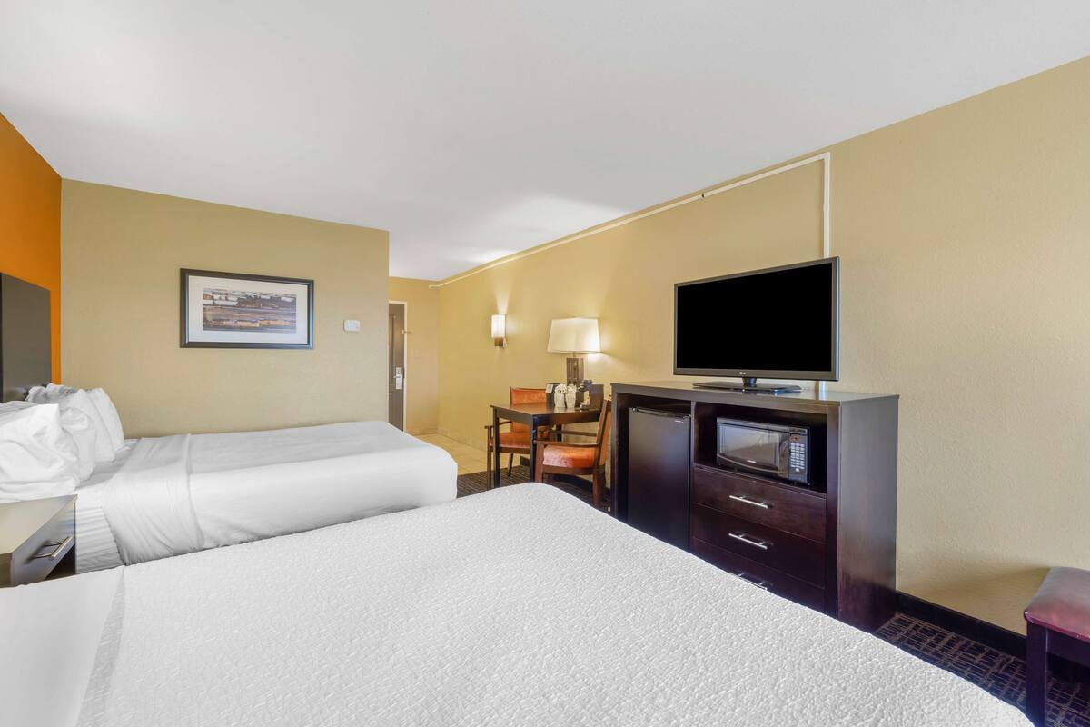 A hotel room with two beds, a desk with a television, a chair, and a lamp.