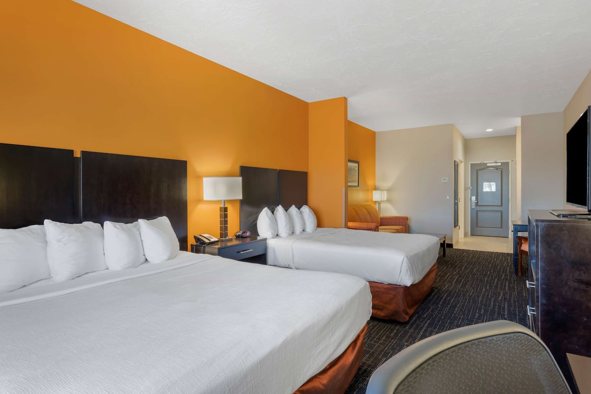 A hotel room with two beds, a desk, a chair, and a television.