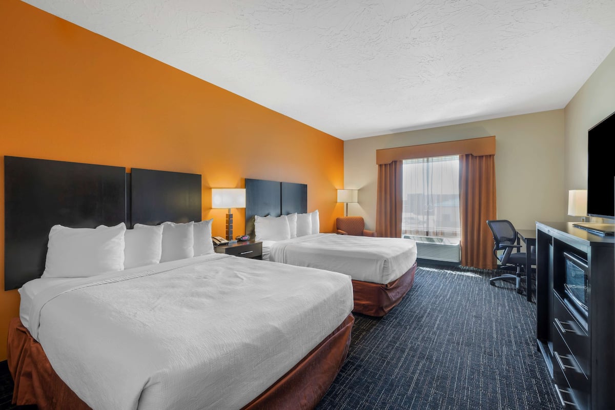 A hotel room with two beds, a desk, a TV, and a window with curtains.