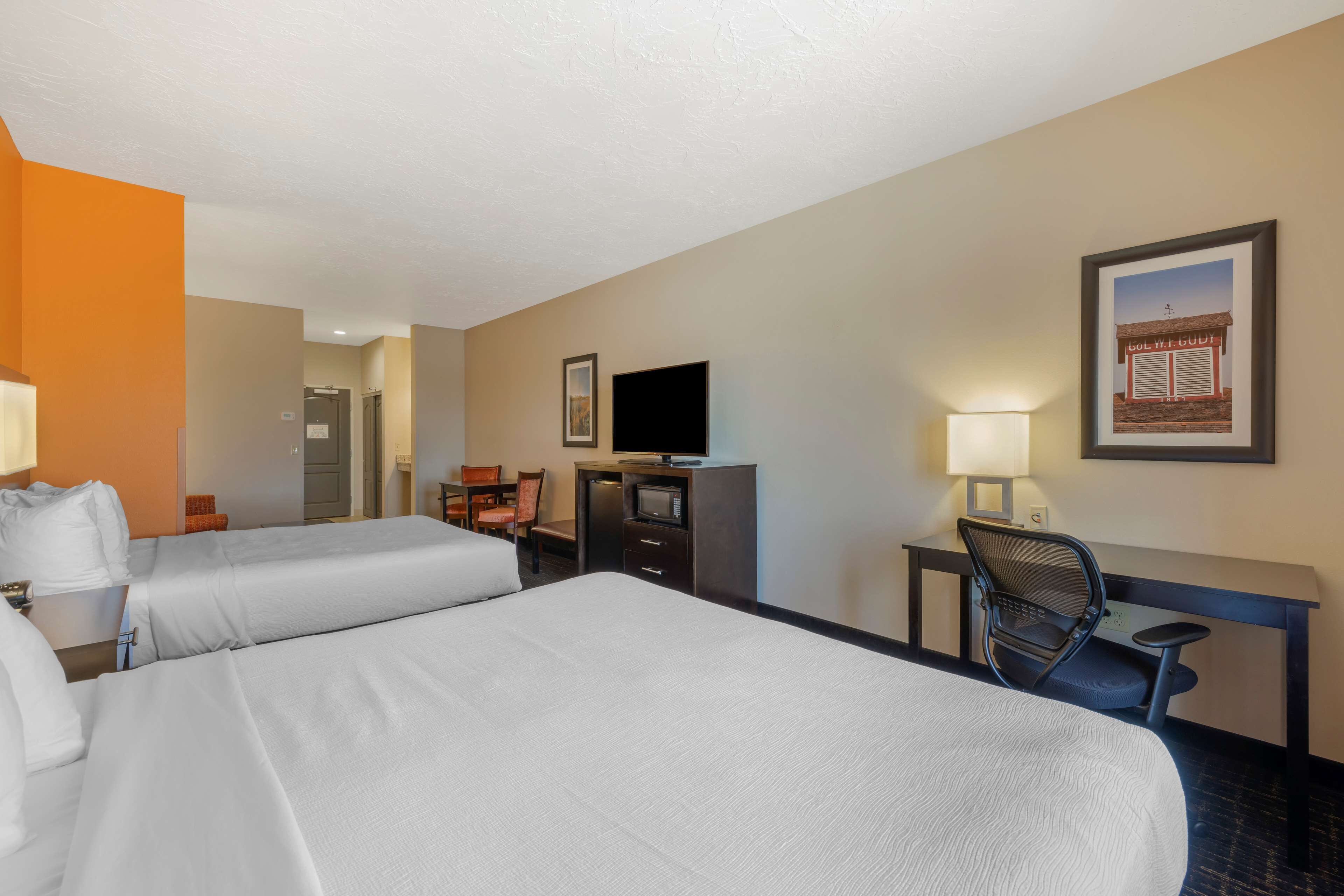 A hotel room with two beds, a desk with a chair, a television, and a framed picture on the wall.
