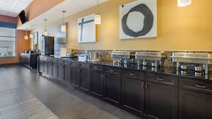 A modern kitchen with dark cabinets, a long counter, and various appliances. There are hanging pendant lights and artwork on the walls. - Best Western Plus North Platte Inn & Suites (North Platte)