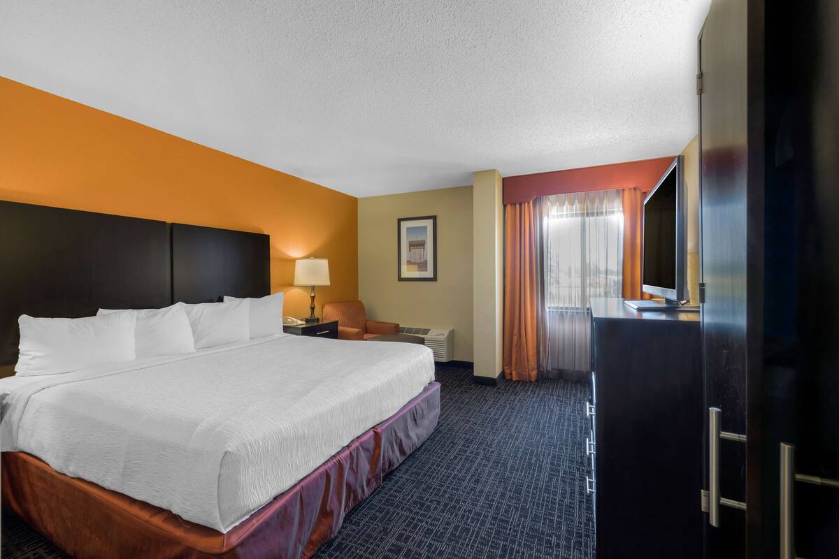 A hotel room with a large bed, a desk with a lamp, a chair, a television, and a wardrobe.