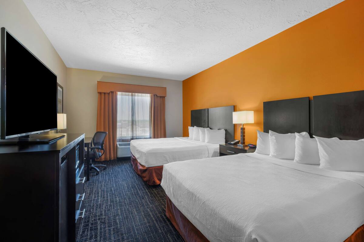 A hotel room with two beds, a TV, a desk, and a window with curtains.