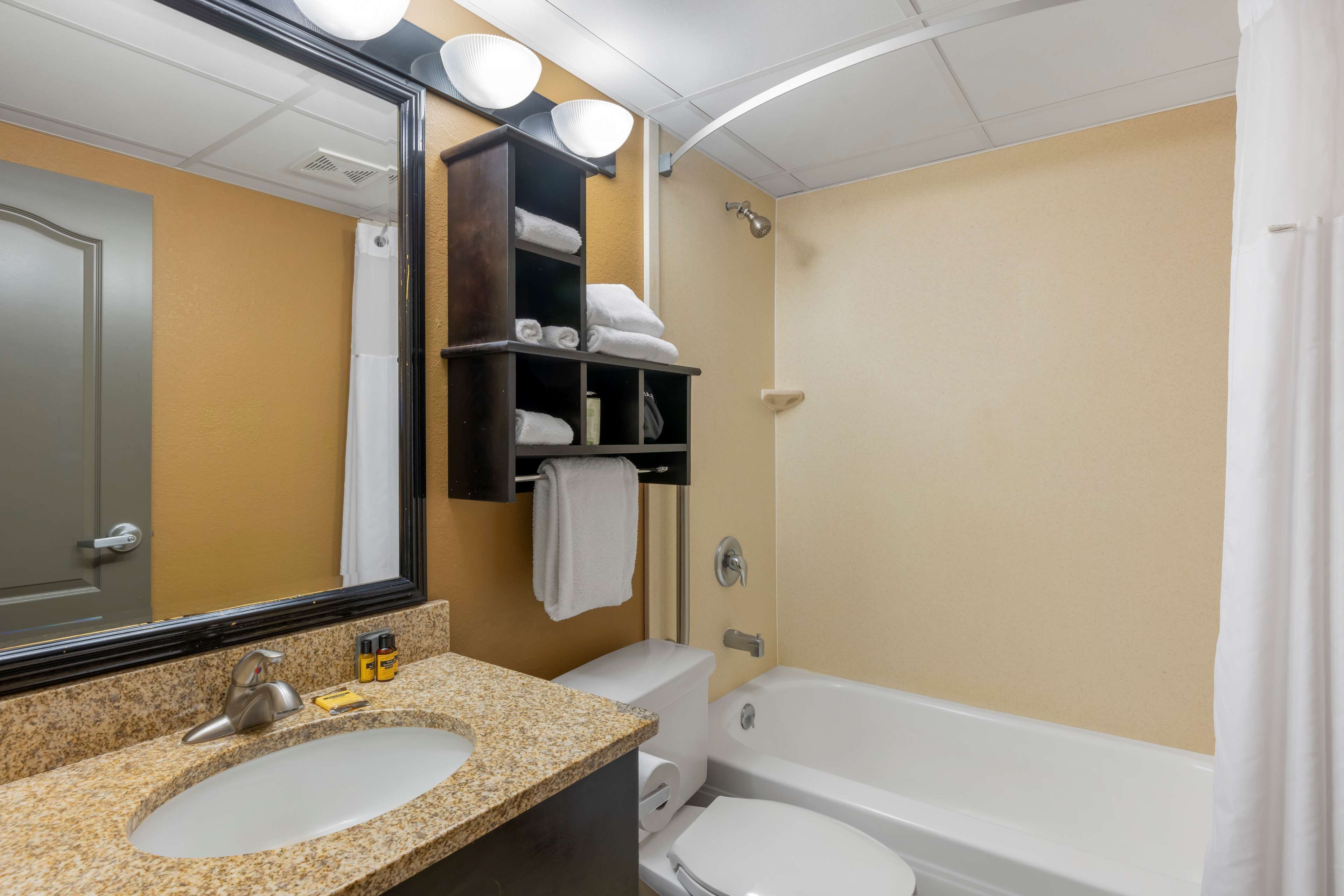 A bathroom with a sink, toilet, and bathtub. There are shelves with towels and toiletries.