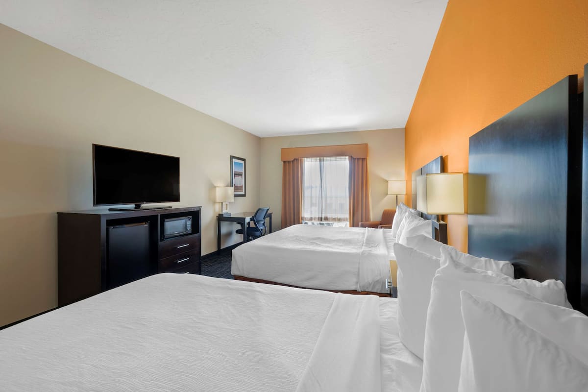 A hotel room with two beds, a desk, a television, and a window with curtains.