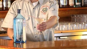En bartender ved en bar med et udvalg af flasker med spiritus i baggrunden.